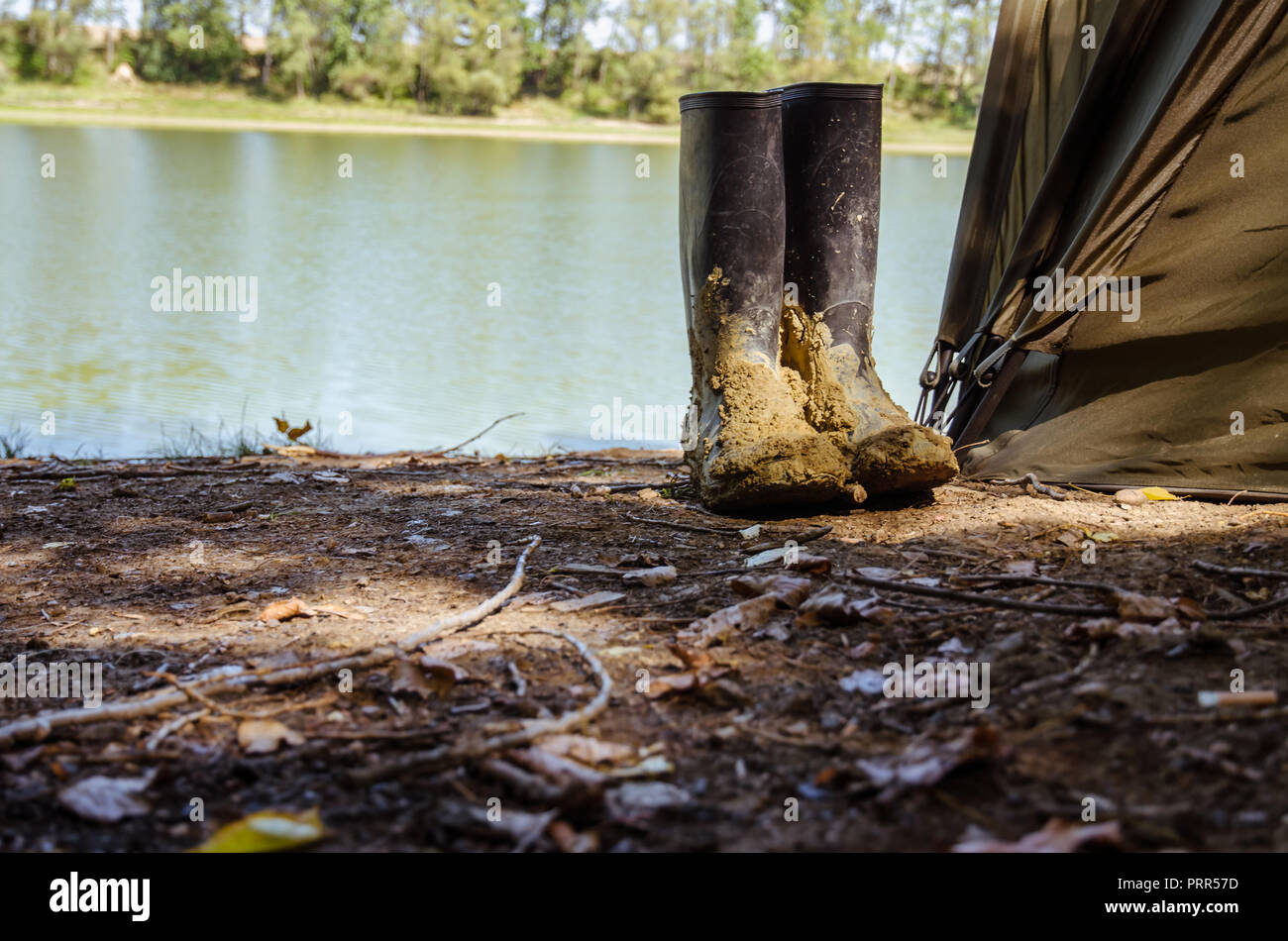 Des bottes debout à côté de la tente de pêche par la rivière Banque D'Images