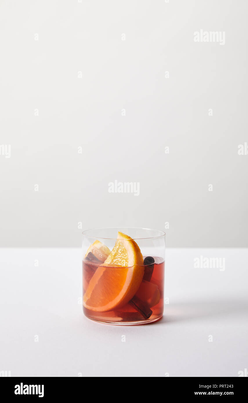 Vue rapprochée de vin chaud dans le verre avec des morceaux d'orange sur la table blanche sur fond gris Banque D'Images