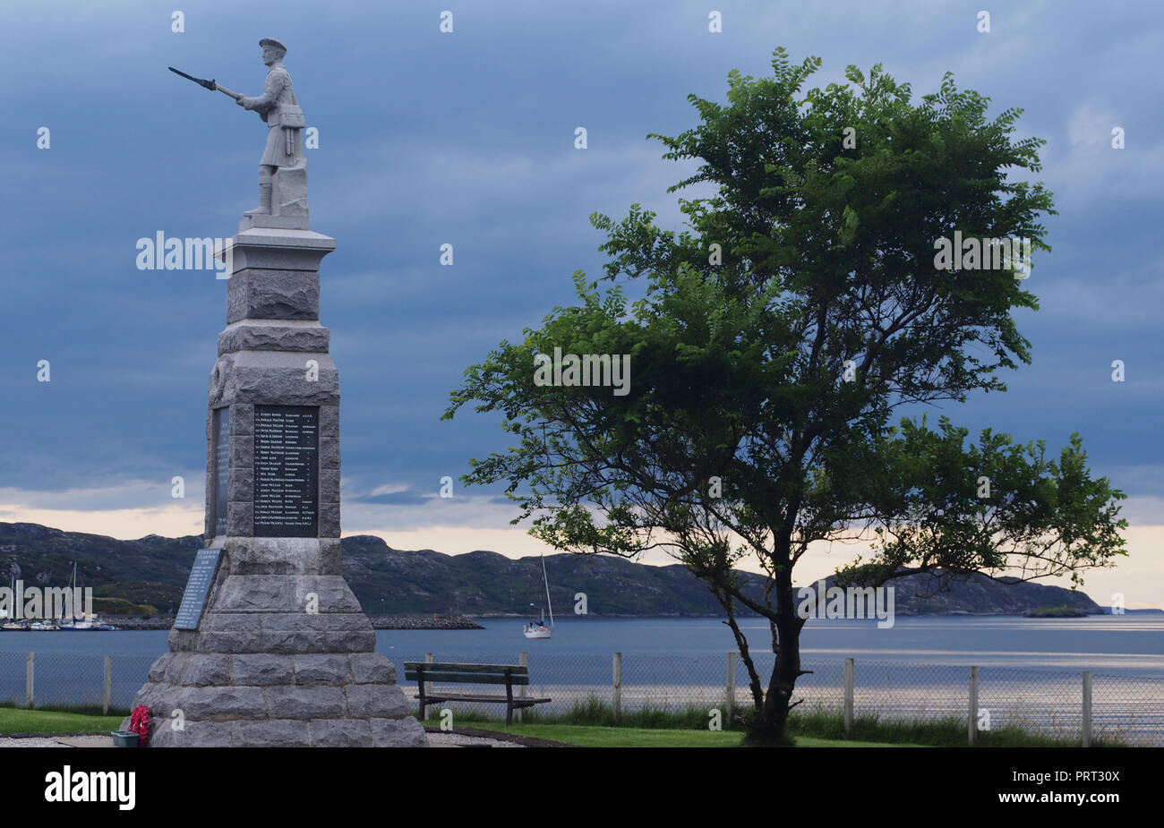 Une vue de Lochinver, l'Écosse, de l'autre côté de la mer du port avec une guerre mondiale un homme d'infanterie avec memorial sur le dessus et d'arbres en premier plan Banque D'Images