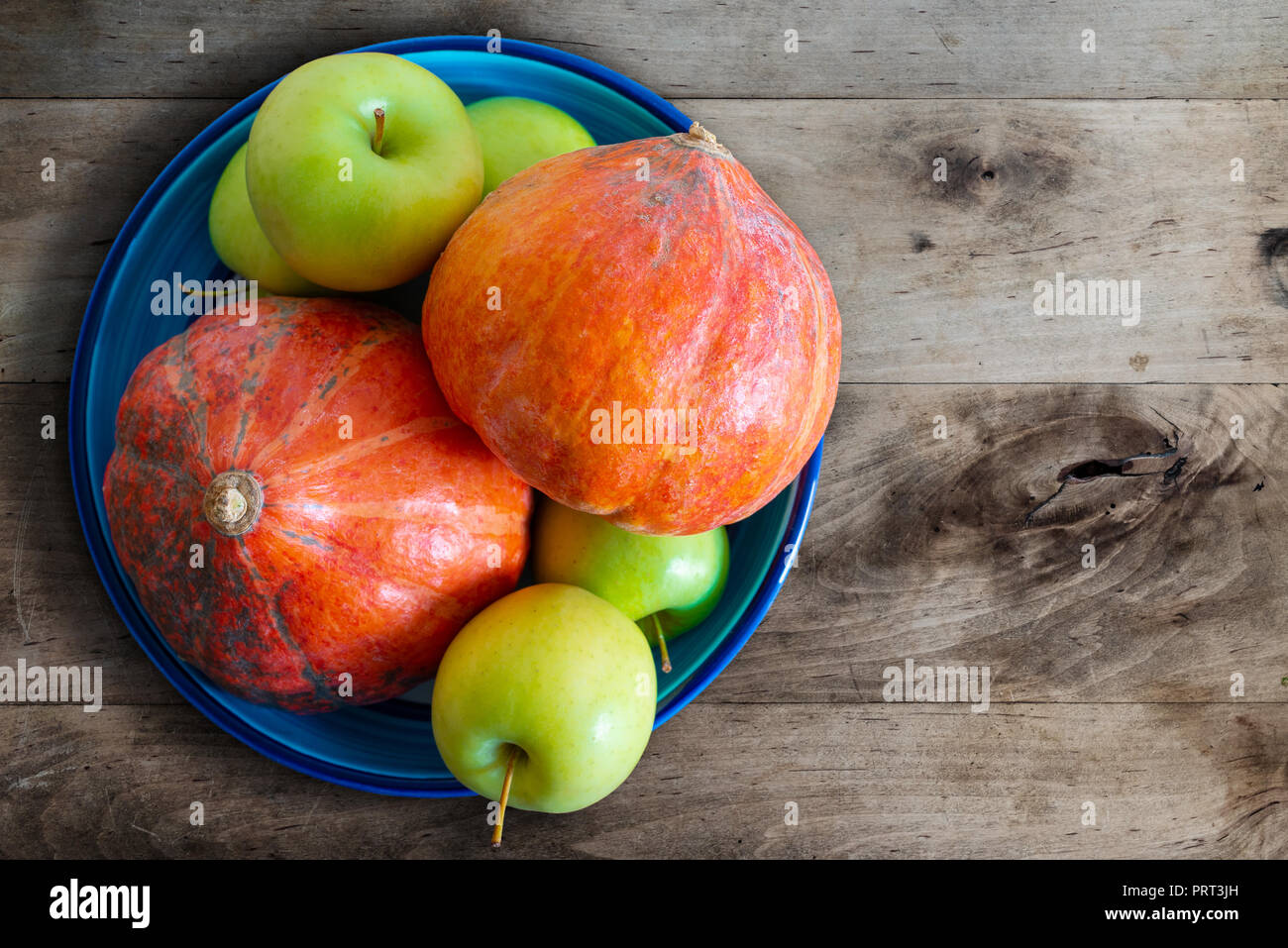 Les citrouilles et les pommes dans le bol en céramique sur une table de cuisine en bois rustique Banque D'Images