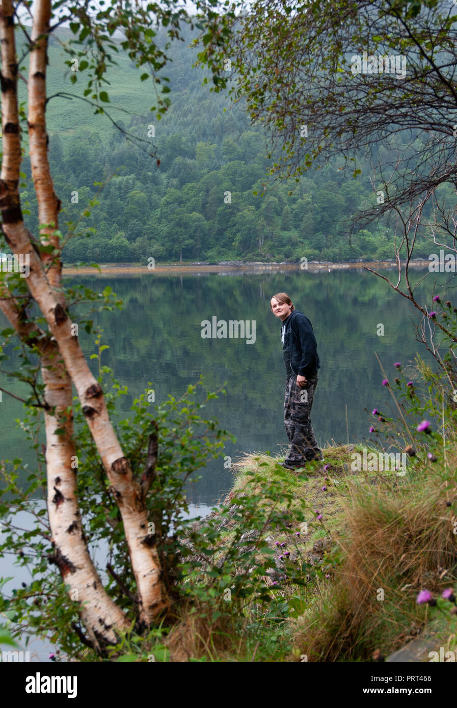 Teenage boy standing on a rock face à la télévision, les eaux calmes réfléchissant des eaux de Kyle of Lochalsh dans les Highlands, Ecosse Banque D'Images