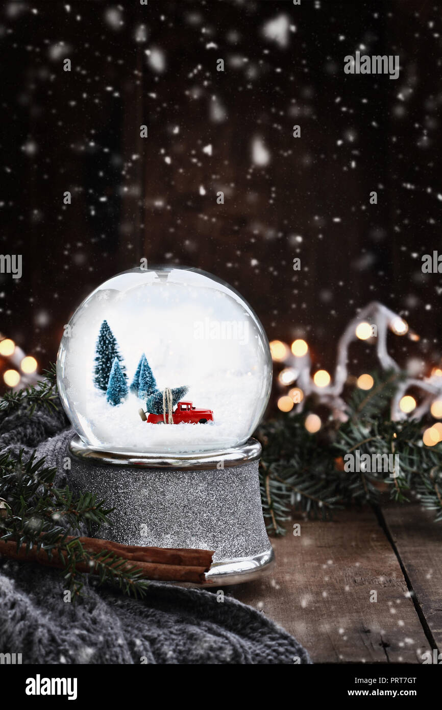 L'image rustique d'un globe de neige avec de vieux pick up tuck transportant un arbre de Noël entouré par des branches de pins, des bâtons de cannelle et un foulard gris chaud. Banque D'Images