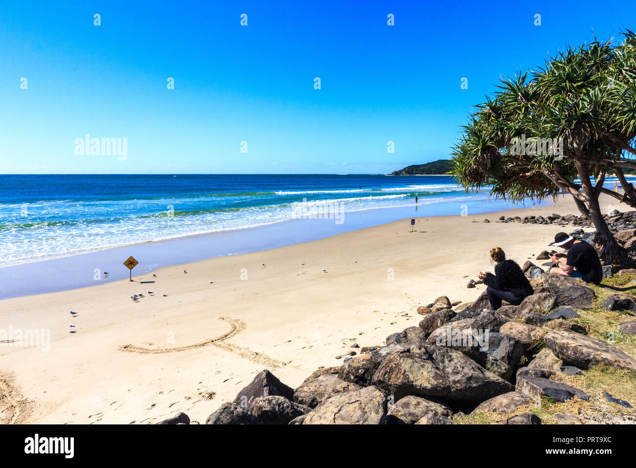 Byron Bay, Australie - 14 mai 2015 : Des gens assis sur des pierres sur la plage. La région est populaire auprès des jeunes. Banque D'Images