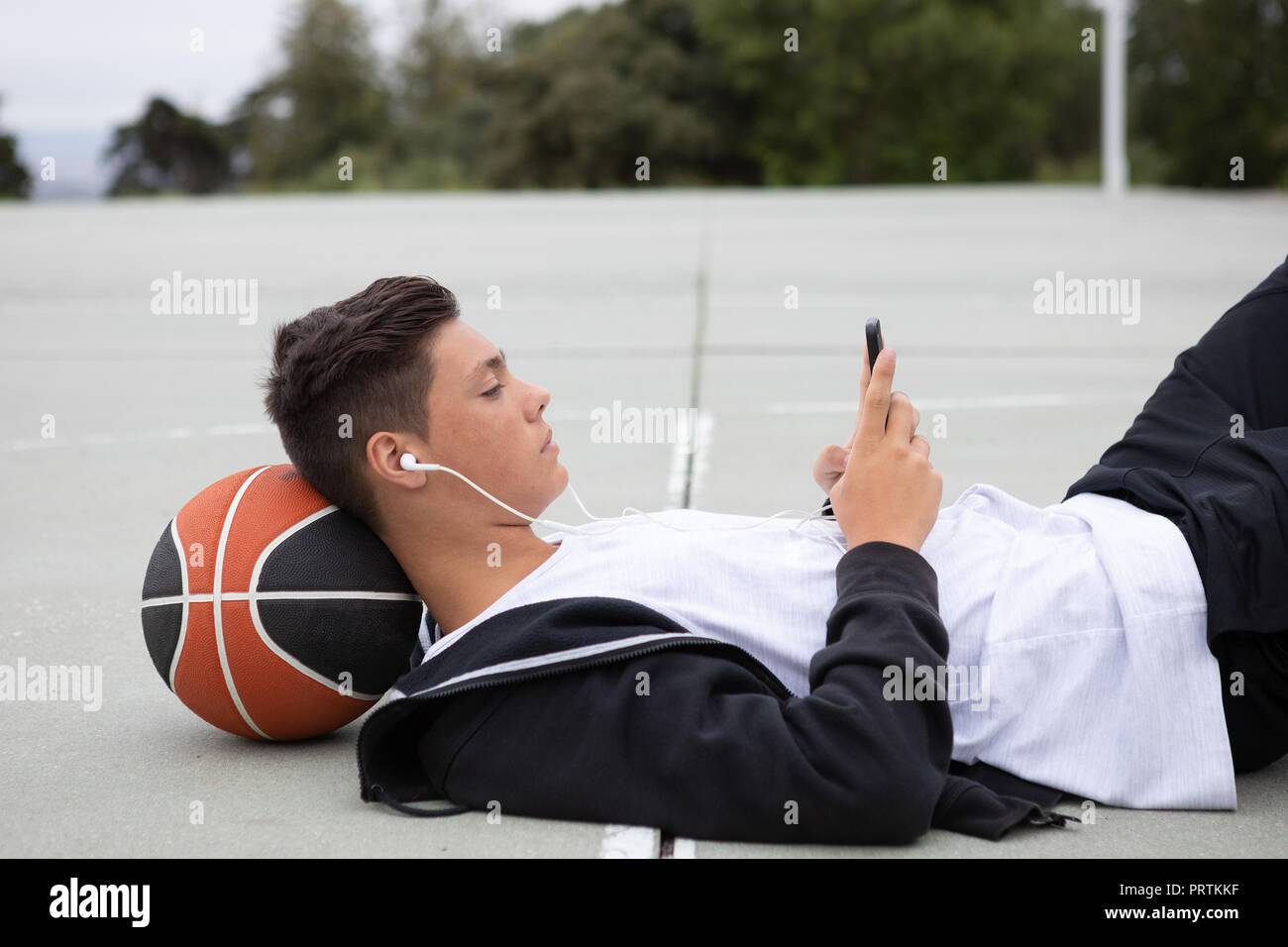 Joueur de basket-ball chez les hommes se trouvant sur un terrain de basket-ball looking at smartphone Banque D'Images