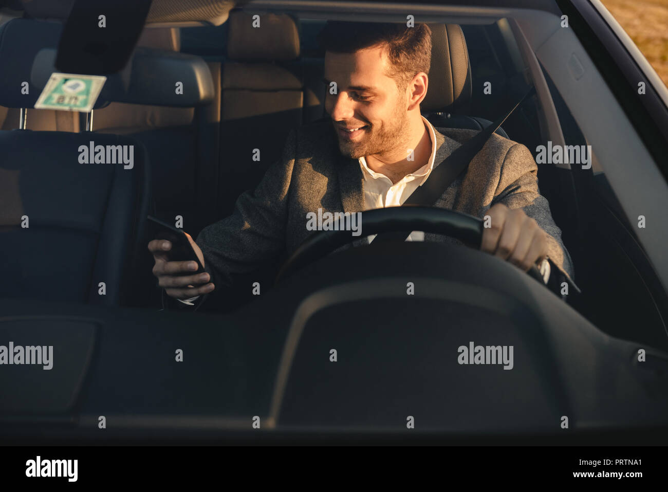 Vue avant du smiling bussinesman litigieux au volant de sa voiture, à l'aide de mobile phone Banque D'Images