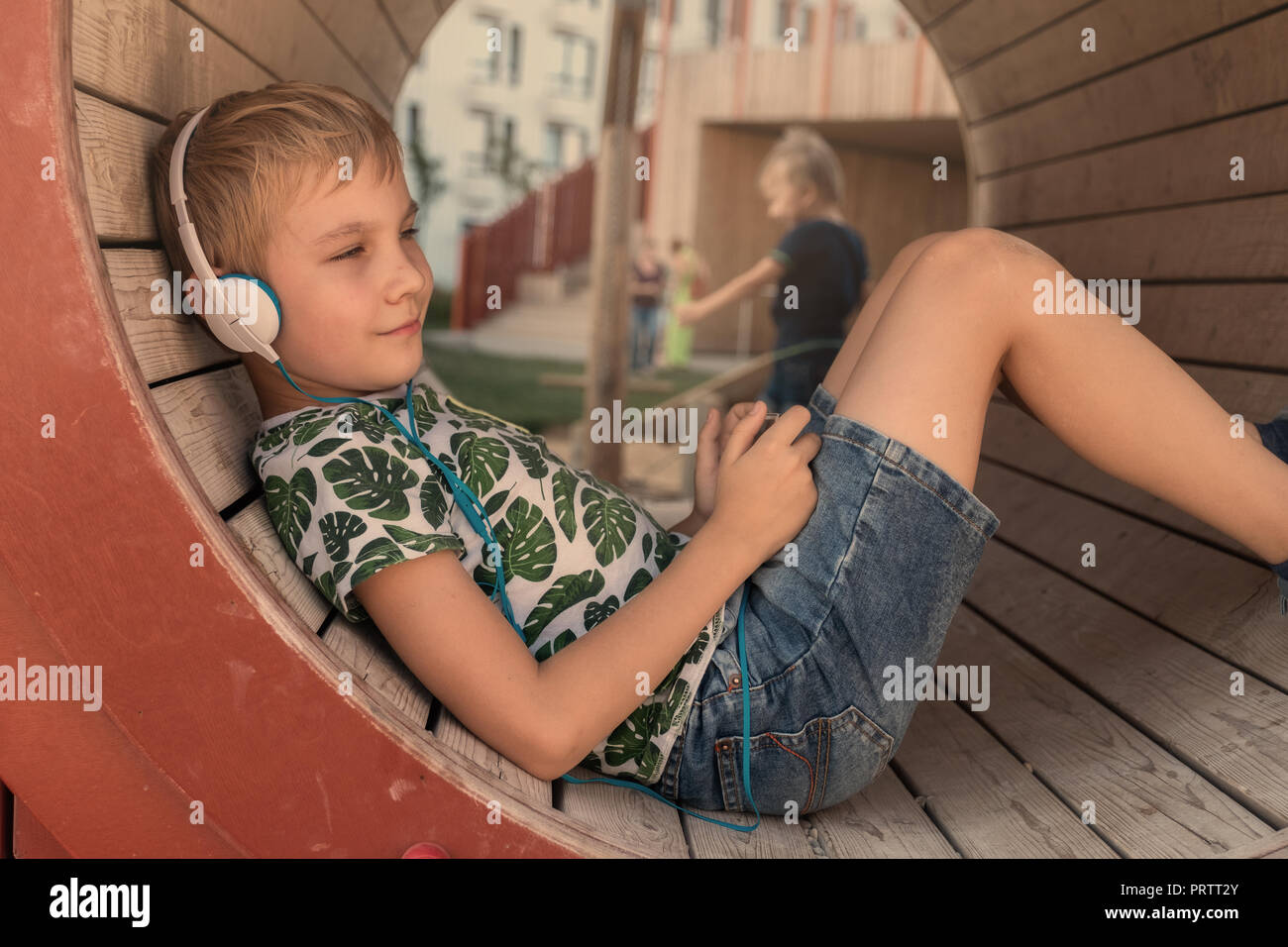 Smiling boy avec le smartphone et l'écoute au casque de la musique ou jouer en plein air jeux Banque D'Images