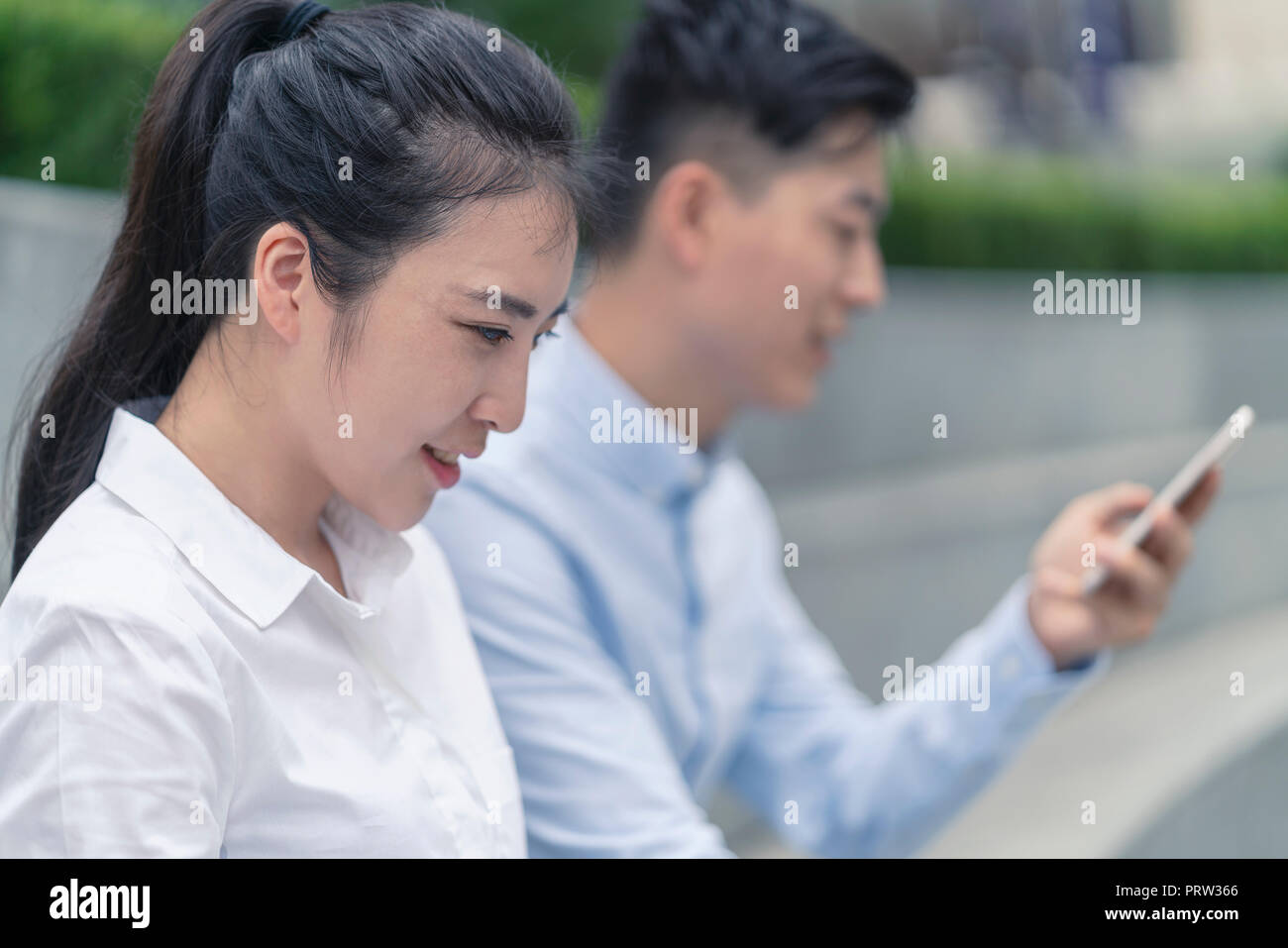 Young businesswoman et man looking at smartphone en ville, Shanghai, Chine Banque D'Images