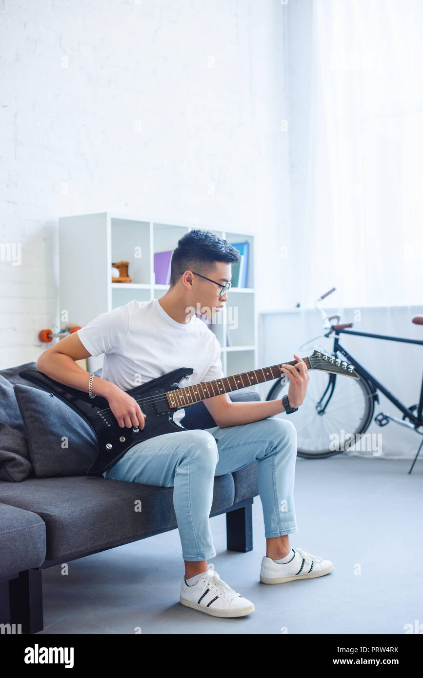 Bel asiatique homme jouant F d'accord sur unplugged guitare électrique à la maison Banque D'Images