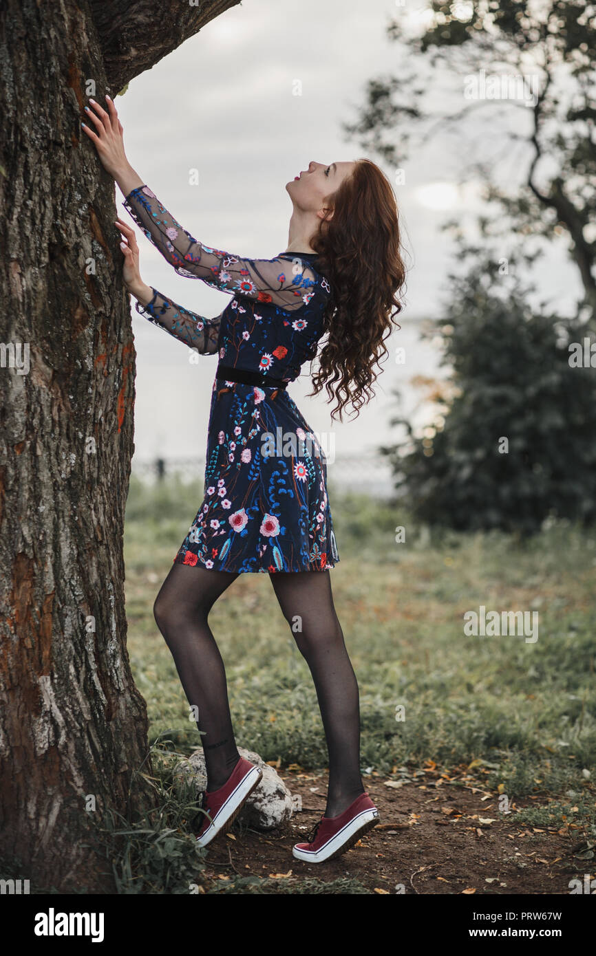 Portrait d'un curly girl dans un parc en automne. Femme svelte avec bénéficiant d'automne nature près de vieil arbre. Concept beauté, santé, forme parfaite. Pleine longueur. Banque D'Images