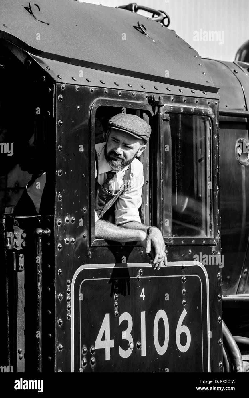 Portrait, noir et blanc gros plan du conducteur du train, à l'intérieur de la cabine de la locomotive à vapeur britannique vintage penchant et regardant la fenêtre du moteur en été soleil. Banque D'Images