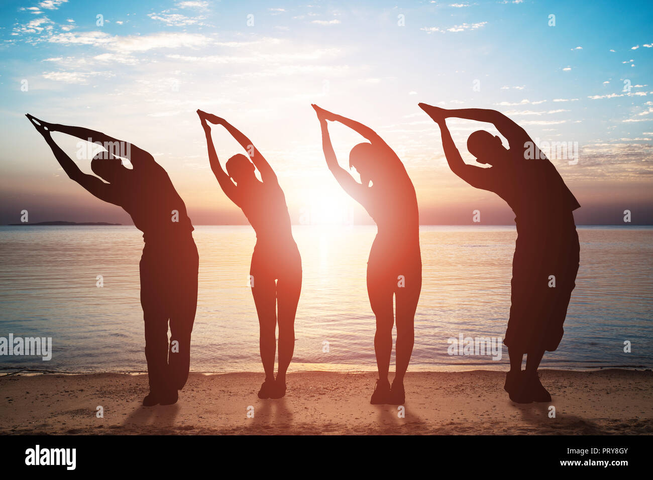 Silhouette de personnes faisant de l'exercice s'étendant sur une plage de sable au coucher du soleil Banque D'Images