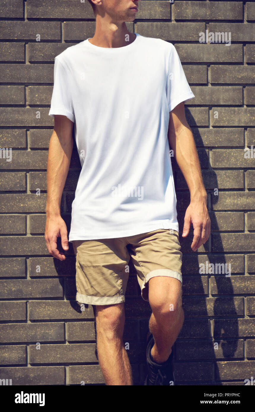 Simulateur de vêtements urbains. Jeune homme debout sur un mur en arrière-plan un T-shirt blanc et un short marron. Template design prêt pour vous Banque D'Images