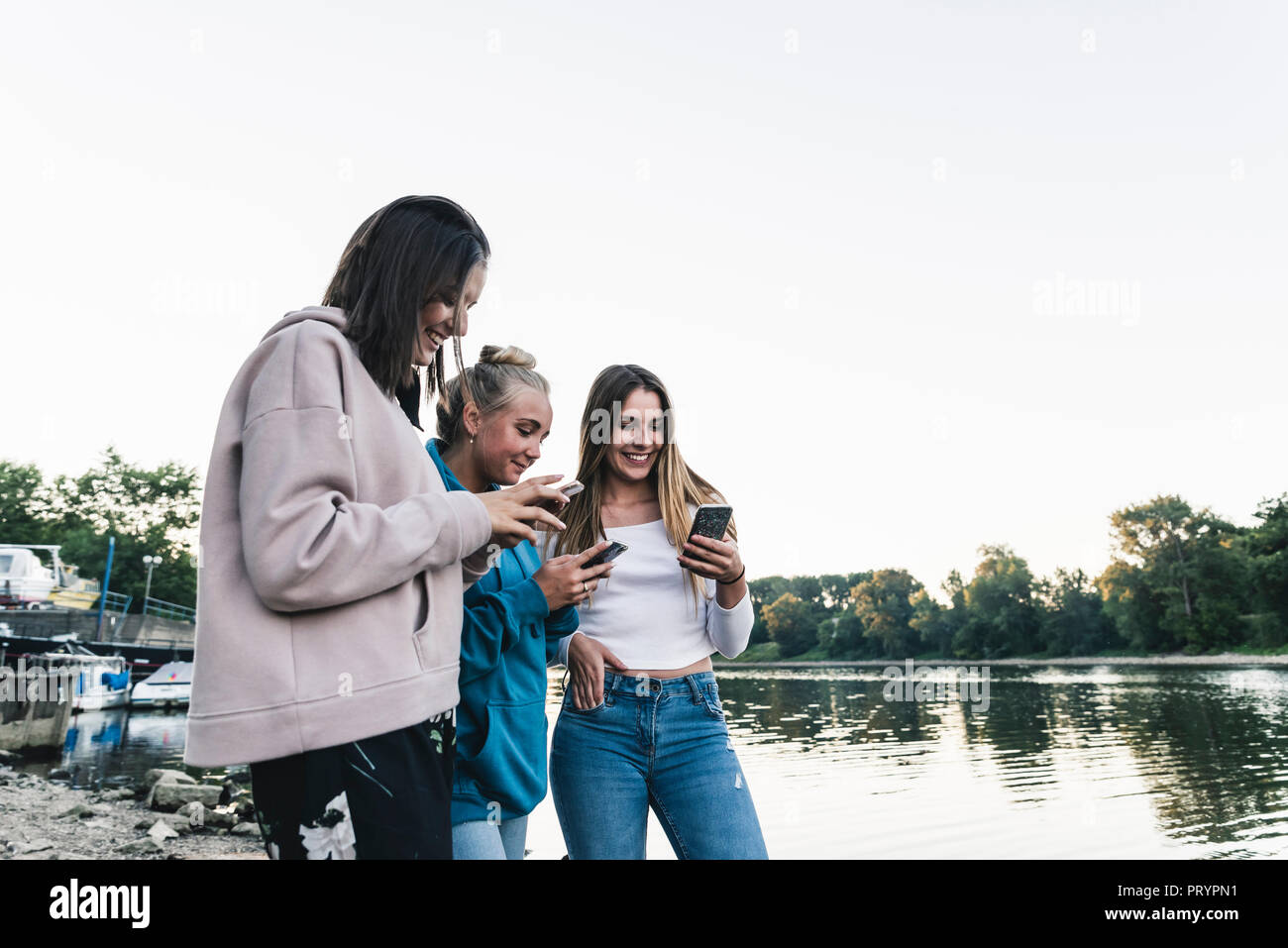 Trois jeunes femmes l'utilisation de téléphones cellulaires au Riverside Banque D'Images