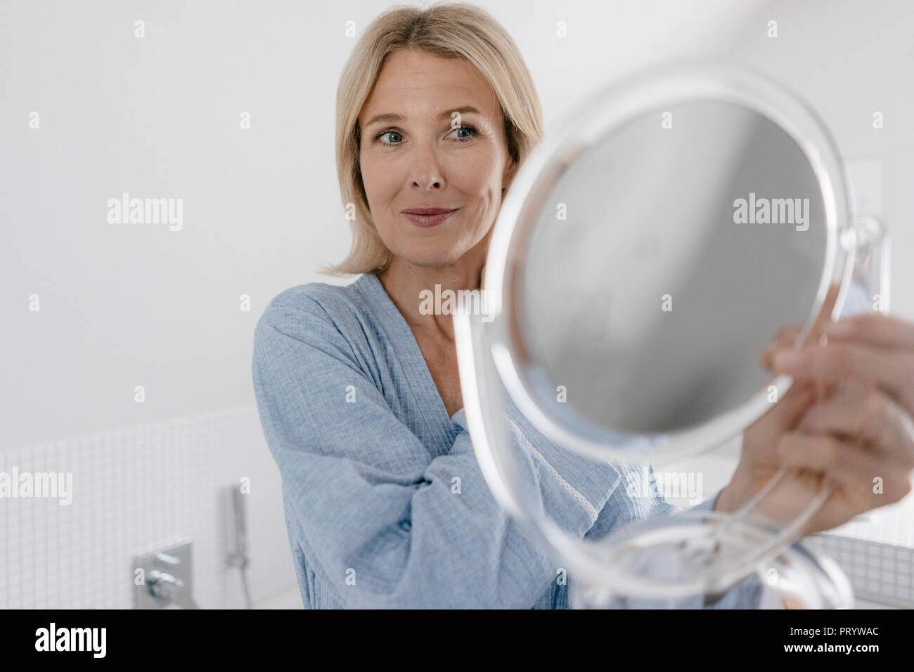 Femme mature à la recherche de miroir de maquillage dans la salle de bains Banque D'Images