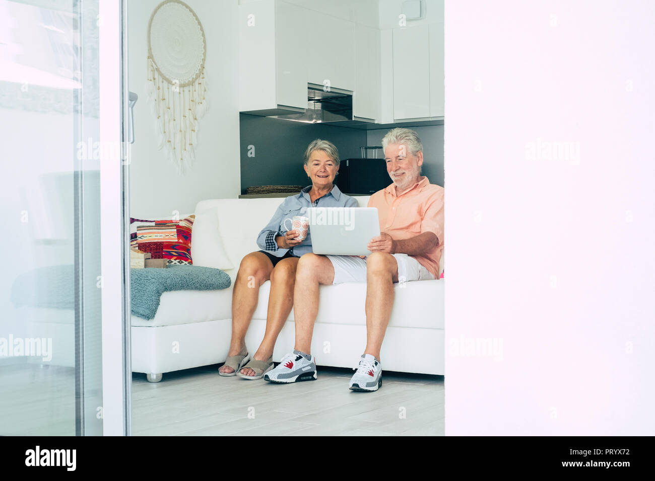 Senior adult caucasian couple les gens s'asseoir sur le canapé à la maison utilisent la technologie et internet avec un ordinateur portable ensemble. sourire et se détendre ensemble dans un e Banque D'Images