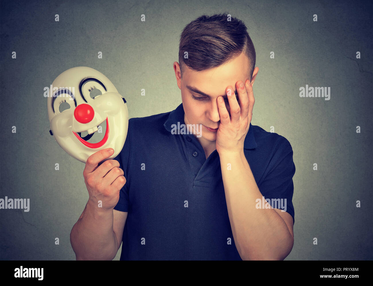 Jeune homme tenant un masque de clown aux couleurs vives et à la colère d'être en dépression et de cacher leurs sentiments Banque D'Images