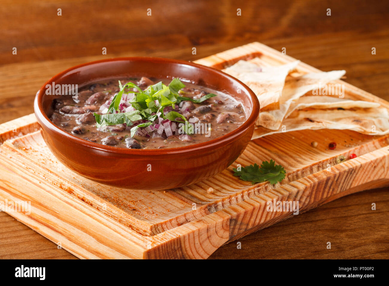 Soupe de haricots rouges, servie sur une planche en bois avec des morceaux de pain. Banque D'Images