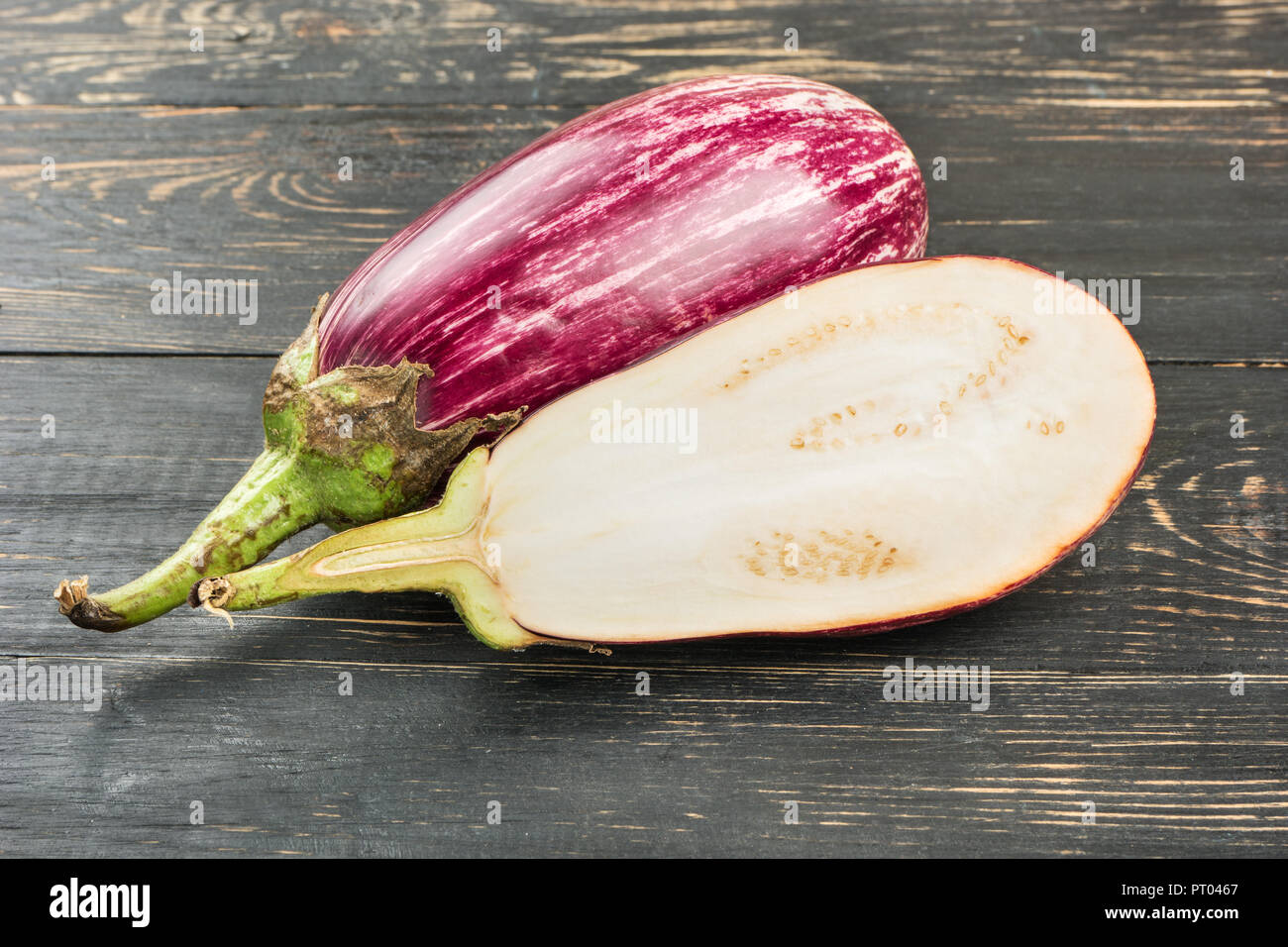 Aubergines crues avec la moitié des graffitis sur fond de bois Banque D'Images