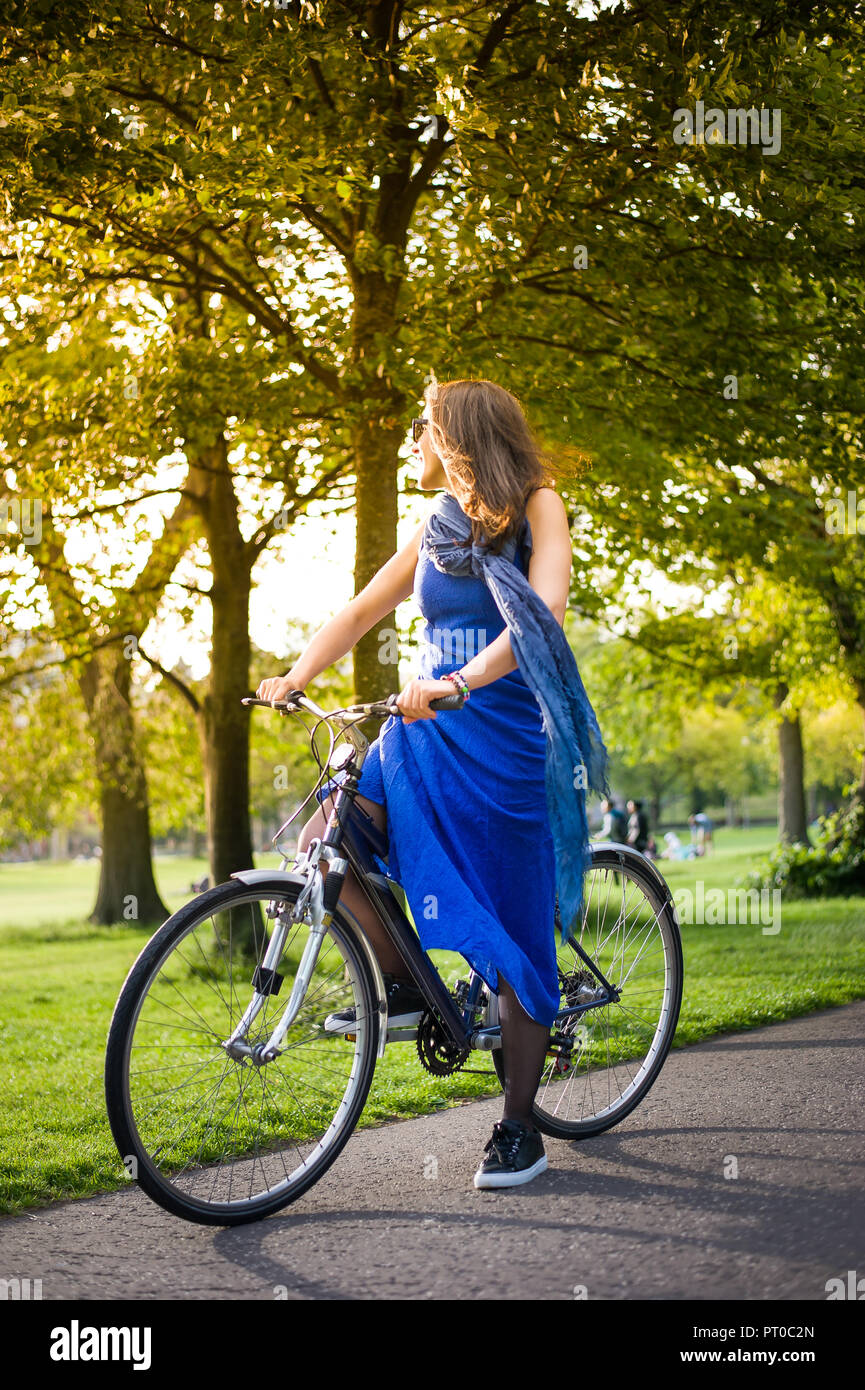 Jeune fille brune en robe bleue et lunettes de soleil sur une bicyclette  bénéficiant de lumière Photo Stock - Alamy