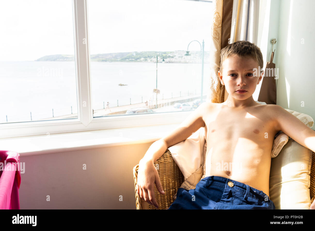 Petit garçon avec l'autisme et le TDAH est assis sur une chaise dans sa chambre d'hôtel avec sa chemise, le syndrome d'Asperger Banque D'Images