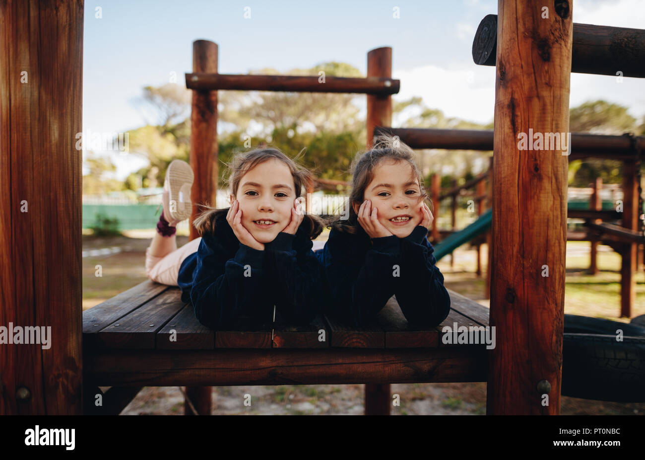 Portrait de deux petites filles heureusement couché sur des structures en bois dans le parc. Deux sœurs s'amuser à l'aire de jeux. Banque D'Images