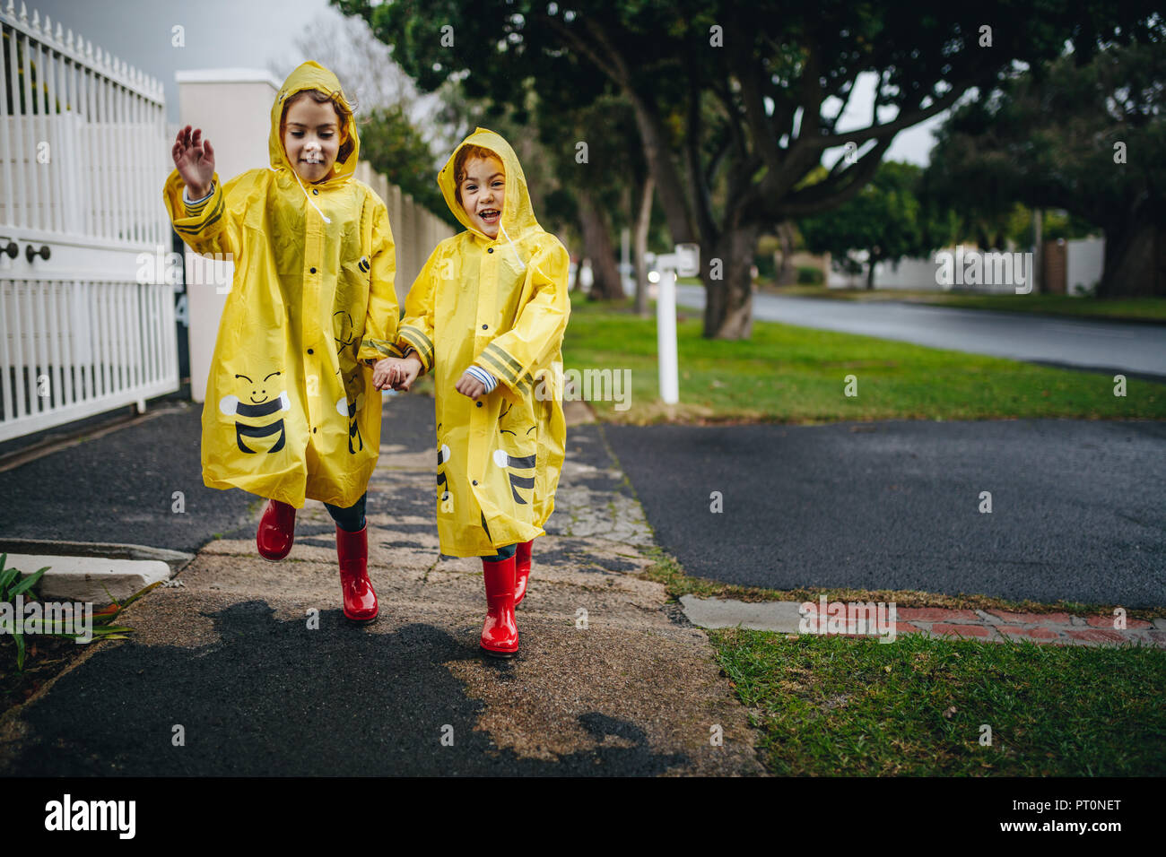 Deux heureux funny girls wearing imperméable jaune et rouge des bottes en caoutchouc. Deux sœurs dans la marche à l'extérieur manteaux imperméables. Banque D'Images