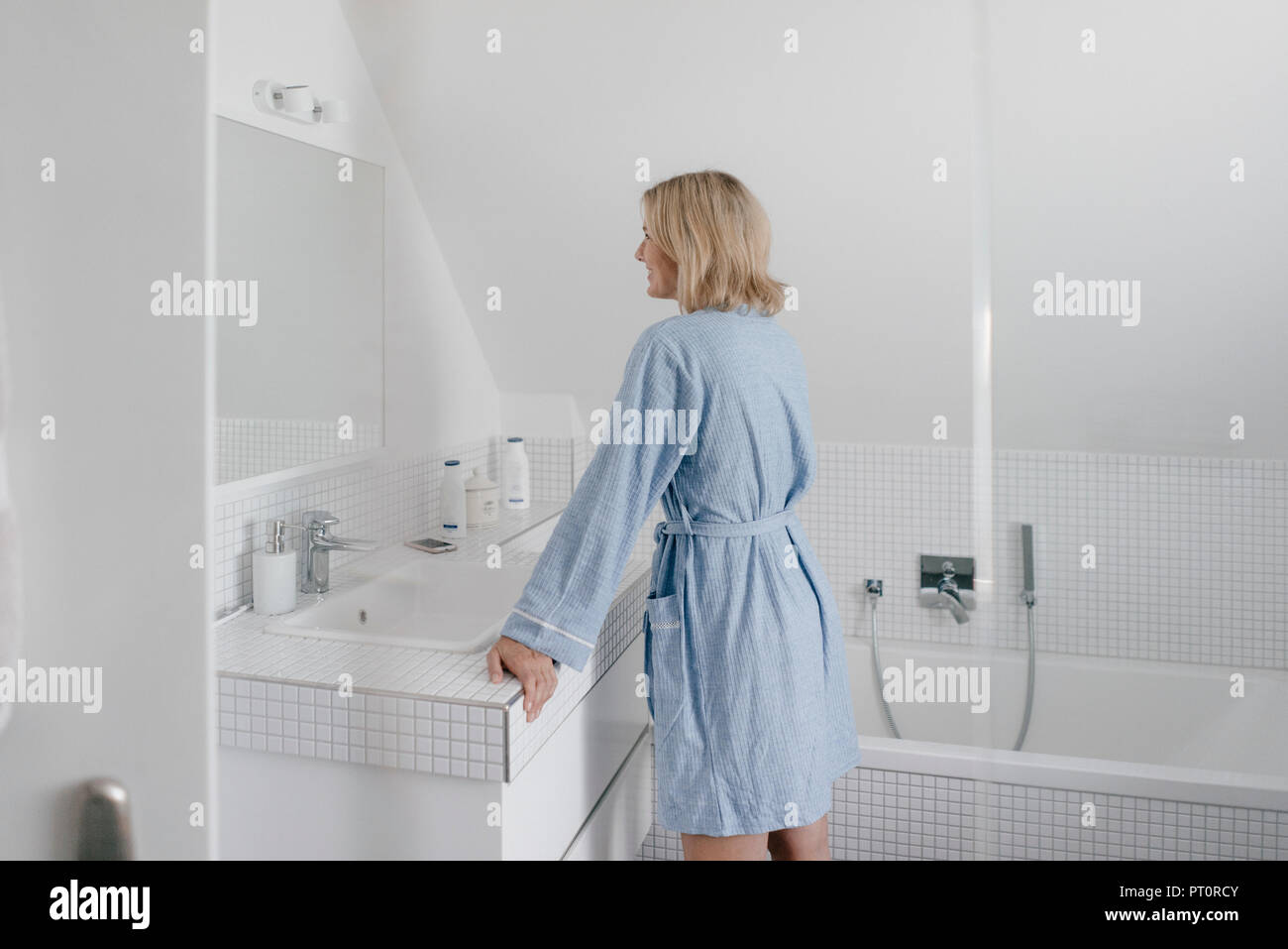 Smiling mature woman en miroir de salle de bains Banque D'Images