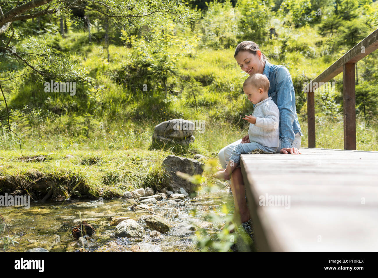 La mère et la fille assis sur pont en bois, ruisseau de montagne Banque D'Images