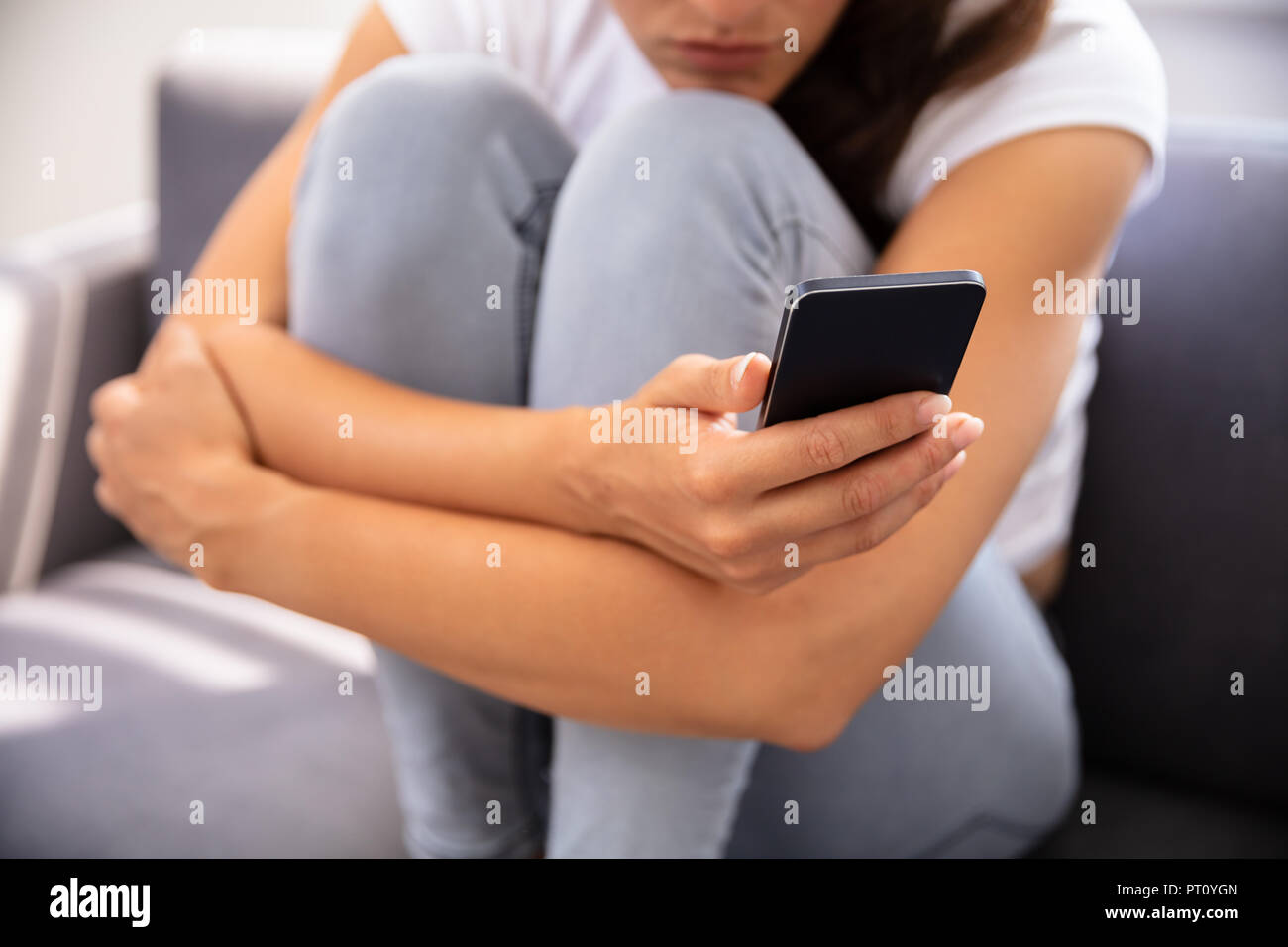 Young Woman Sitting on Sofa Using Smartphone Banque D'Images