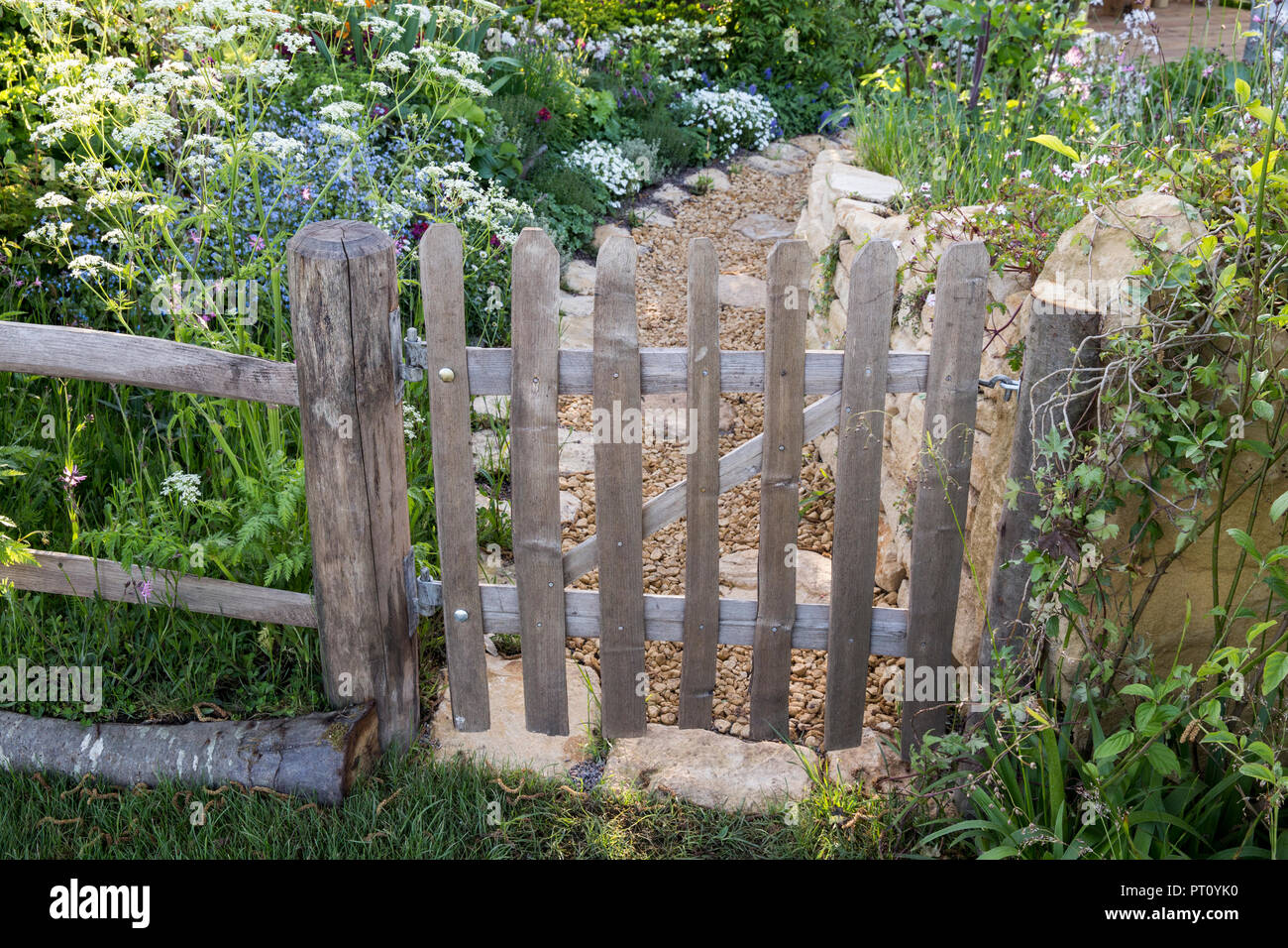 Rustique vieux piquet en bois porte de jardin clôture fleurs sauvages style cottage jardin plantation chemin de gravier Cotswold mur en pierre sèche printemps été Royaume-Uni Banque D'Images