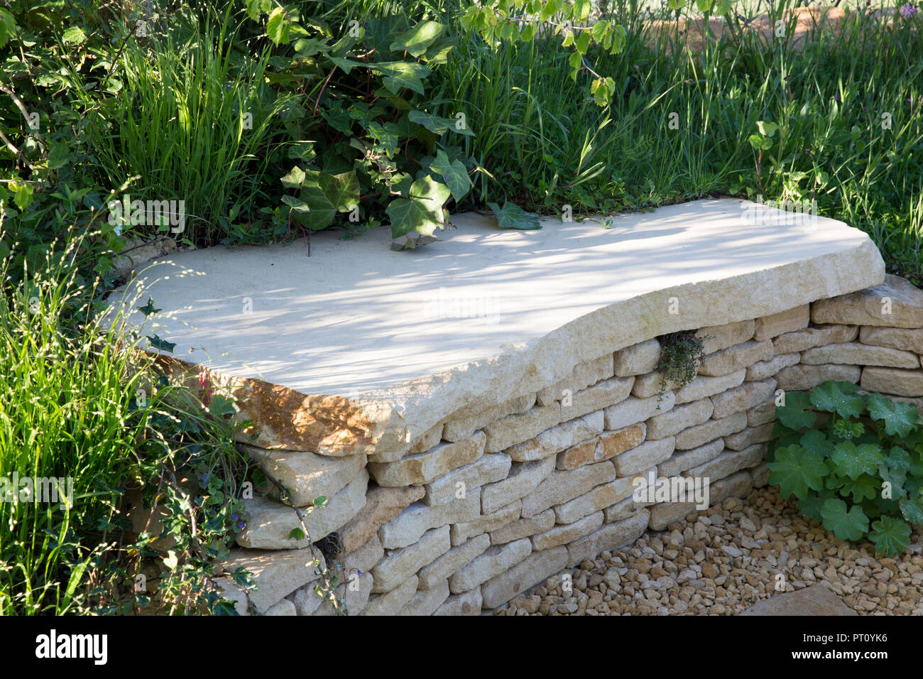 Mur en pierre sèche de Cotswold avec banc de jardin en pierre, chemin de gravier, l'étang de rosée Jardin, Festival du printemps 2018 RHS Malvern Banque D'Images