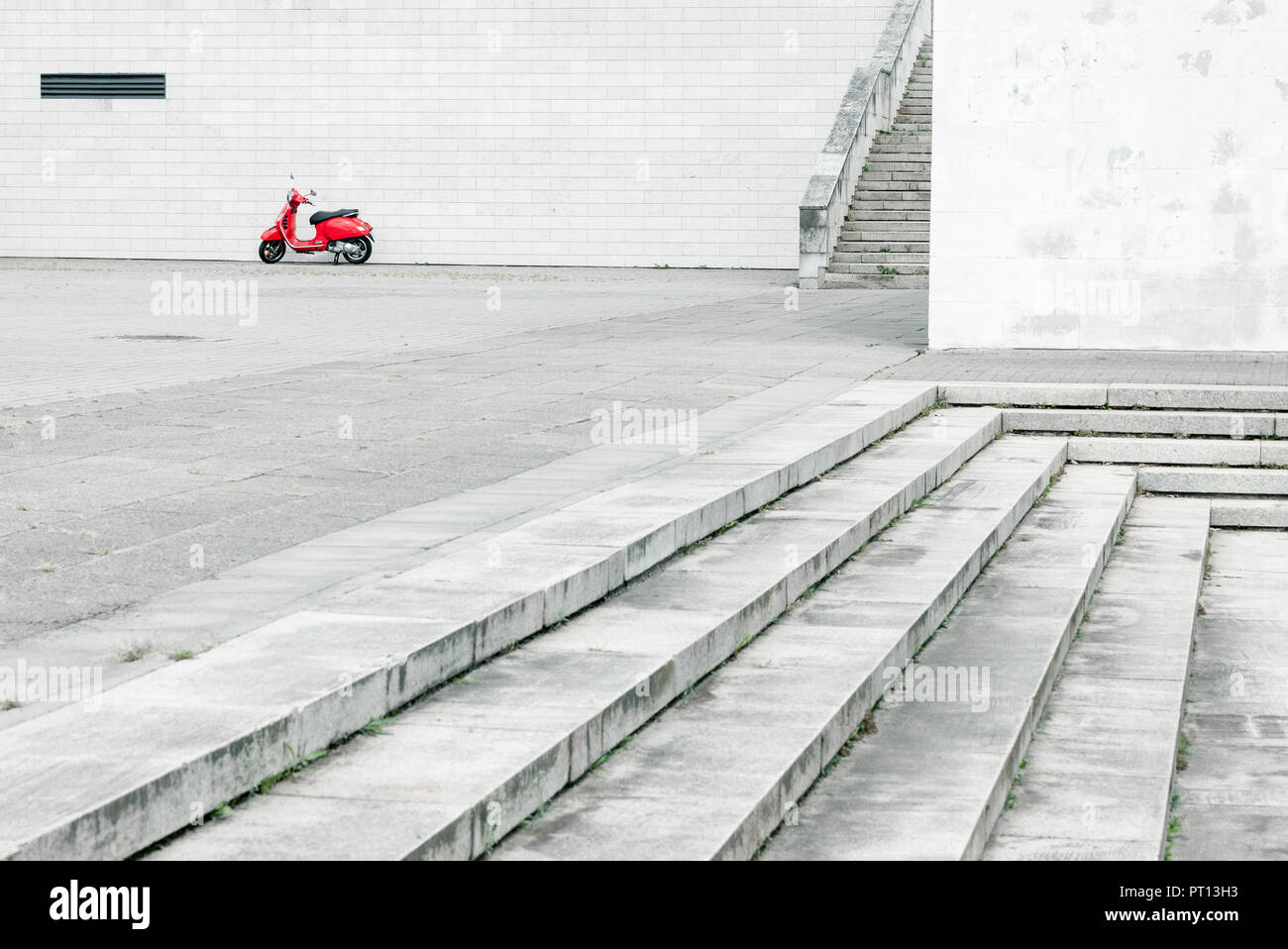 Scooter rouge solitaire contre mur blanc en arrière-plan et abondamment avec de l'environnement urbain en premier plan Banque D'Images