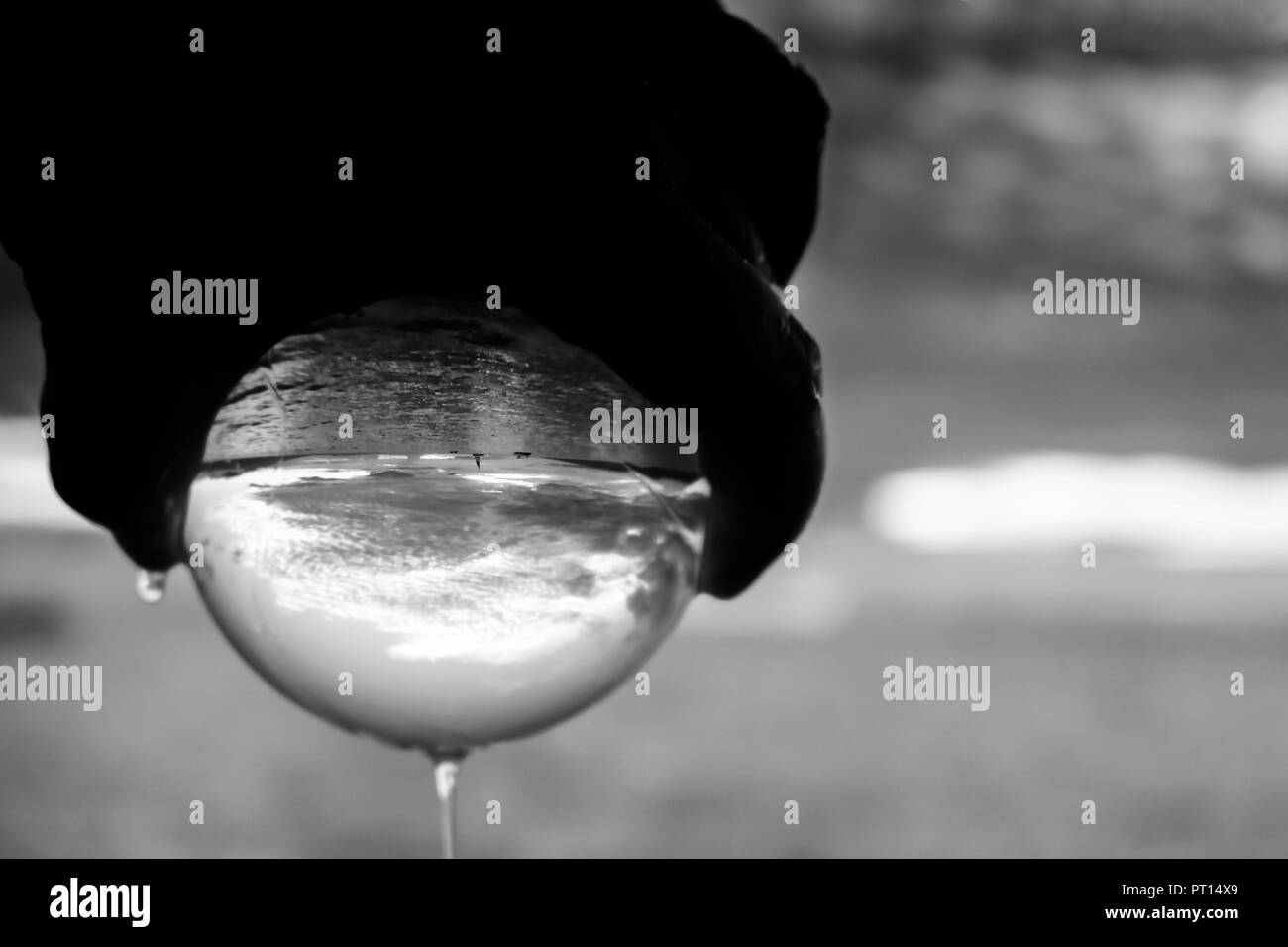 Coucher de soleil paysage marin noir et blanc capturé dans le verre ballon tenu dans la main avec l'écoulement d'eau Banque D'Images