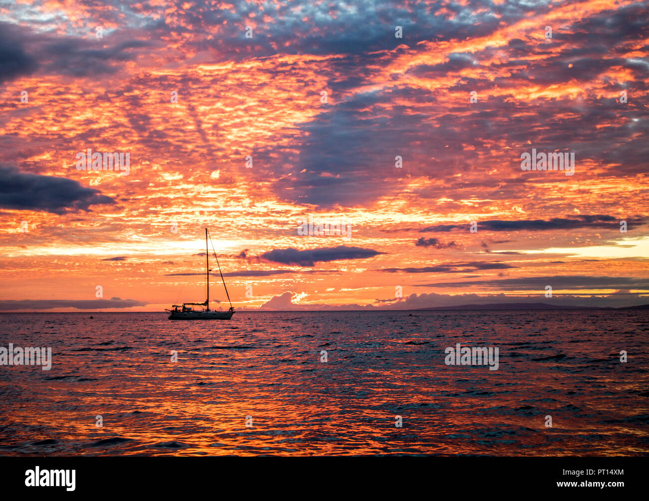 Coucher Soleil nuages orange lumineux ciel de remplissage et de réfléchir sur la surface de l'océan, avec un bateau en silhouette sur l'horizon Banque D'Images