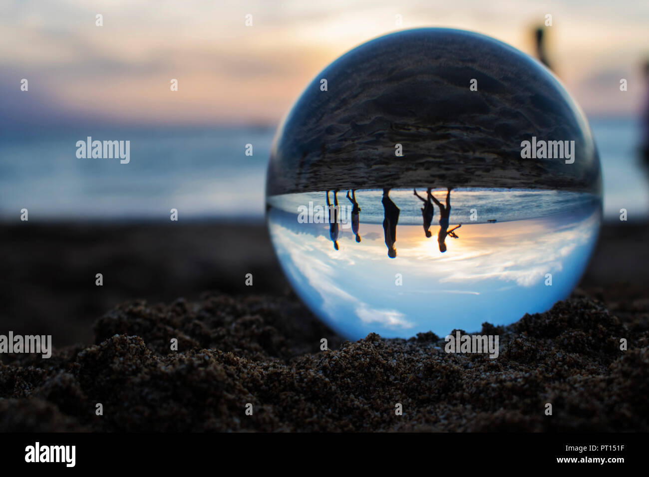 Coucher du soleil sur la plage avec océan et le ciel capturée dans la réflexion dans globe de verre sur le sable avec la famille marche à travers ball en silhouette Banque D'Images