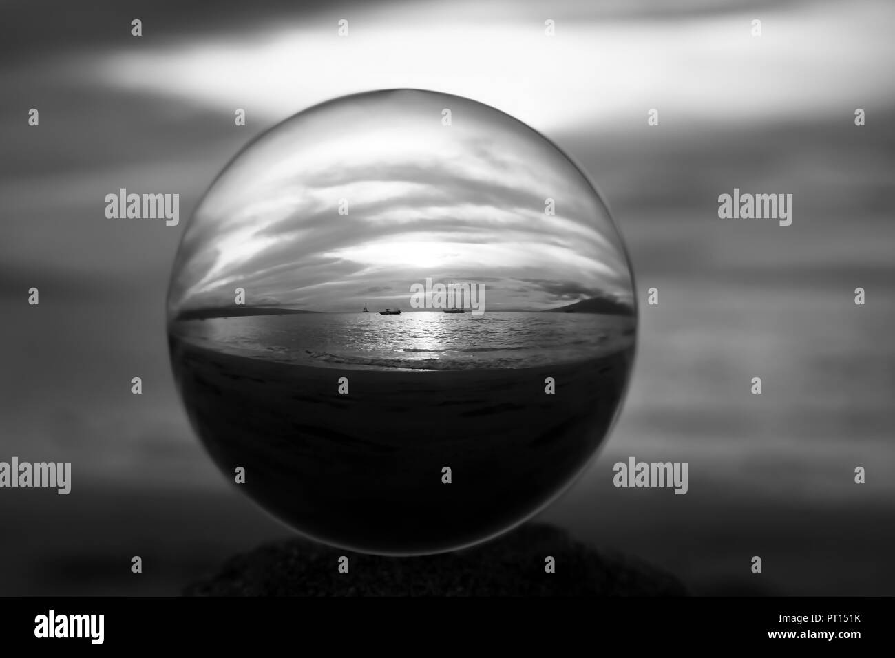 Le noir et blanc sunset seascape de bougies sur l'eau capturée dans close up bille de verre ou globe terrestre Banque D'Images