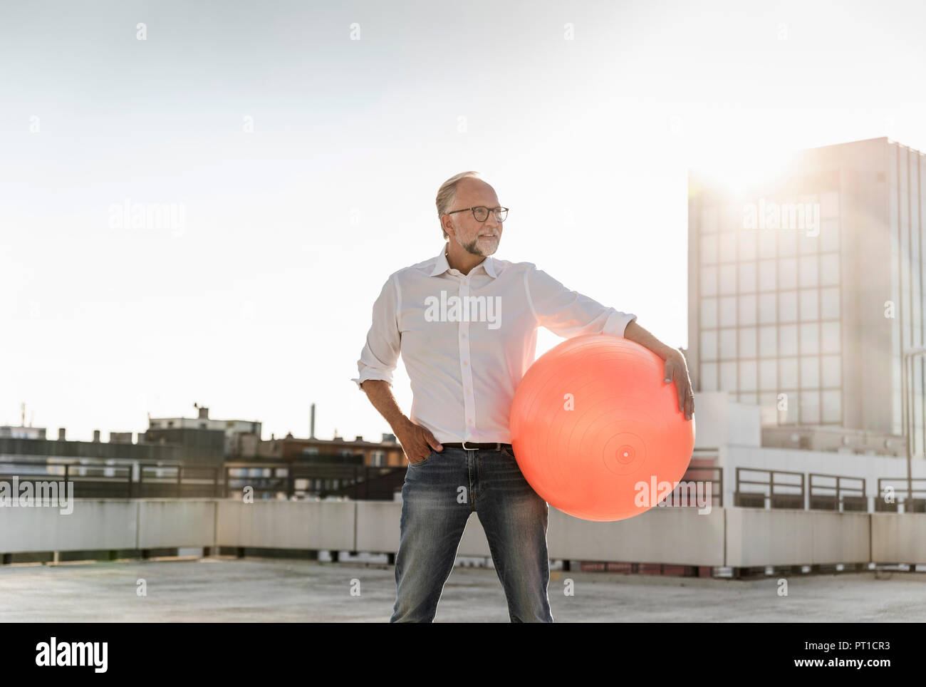 Homme mûr jouant avec orange fitness ball sur le toit d'un immeuble de grande hauteur Banque D'Images
