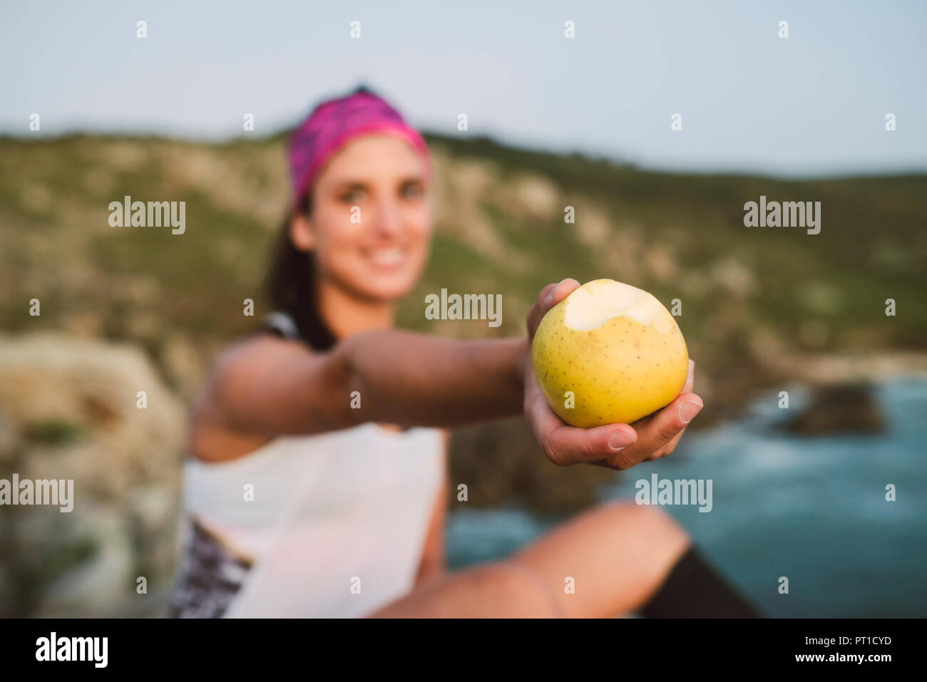 Sportive woman sitting on rocks, holding apple, focus on foreground Banque D'Images