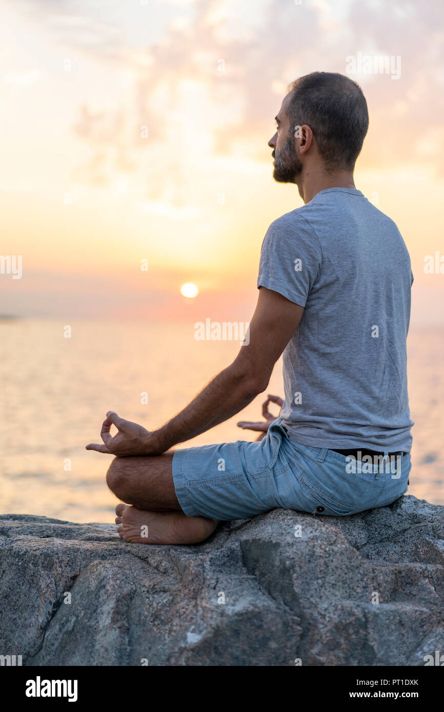 L'Espagne. Homme méditant au lever du soleil, on Rocky beach Banque D'Images