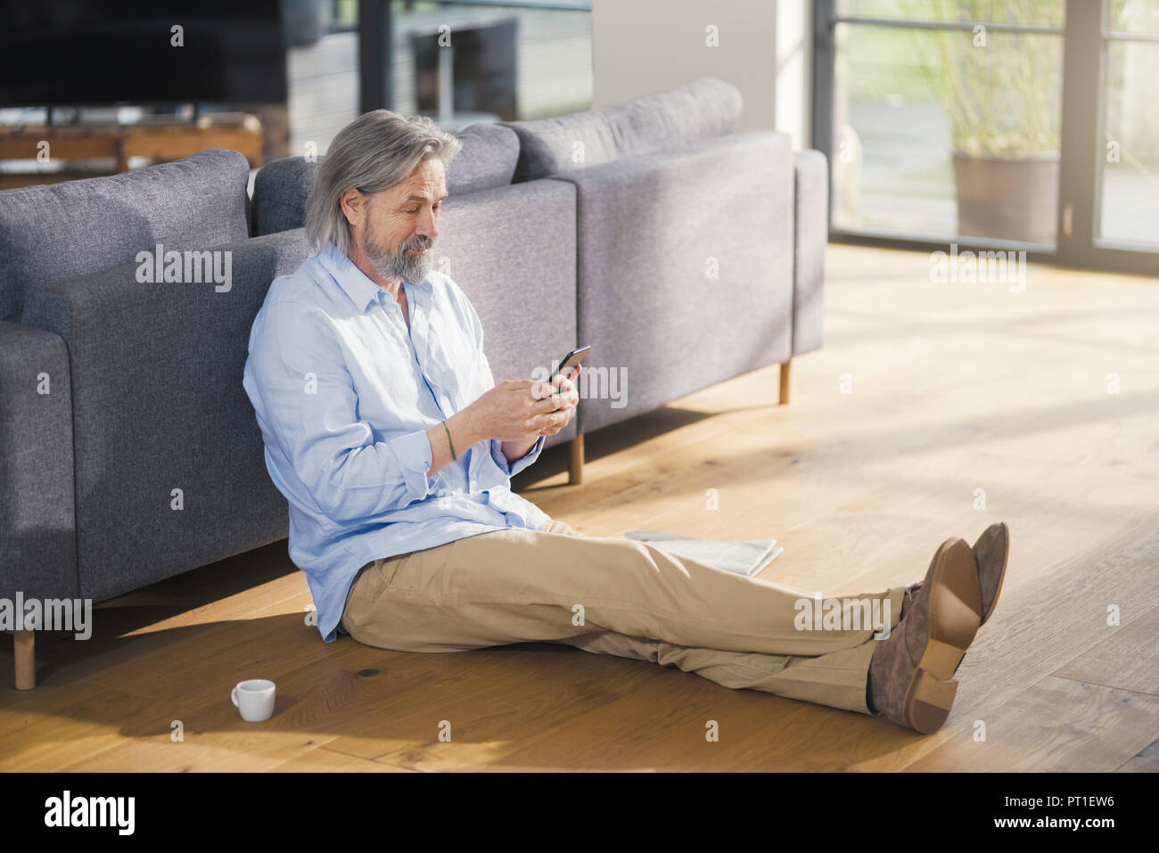 Senior man using smartphone, sitting on floor Banque D'Images
