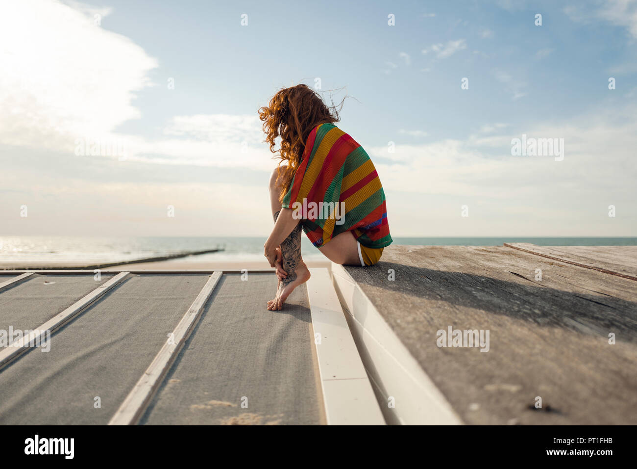 Woman with tattoo accroupi sur planche, regardant la mer Banque D'Images