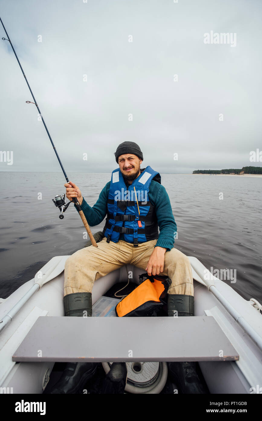 Homme assis sur le bateau de pêche avec canne à pêche Banque D'Images