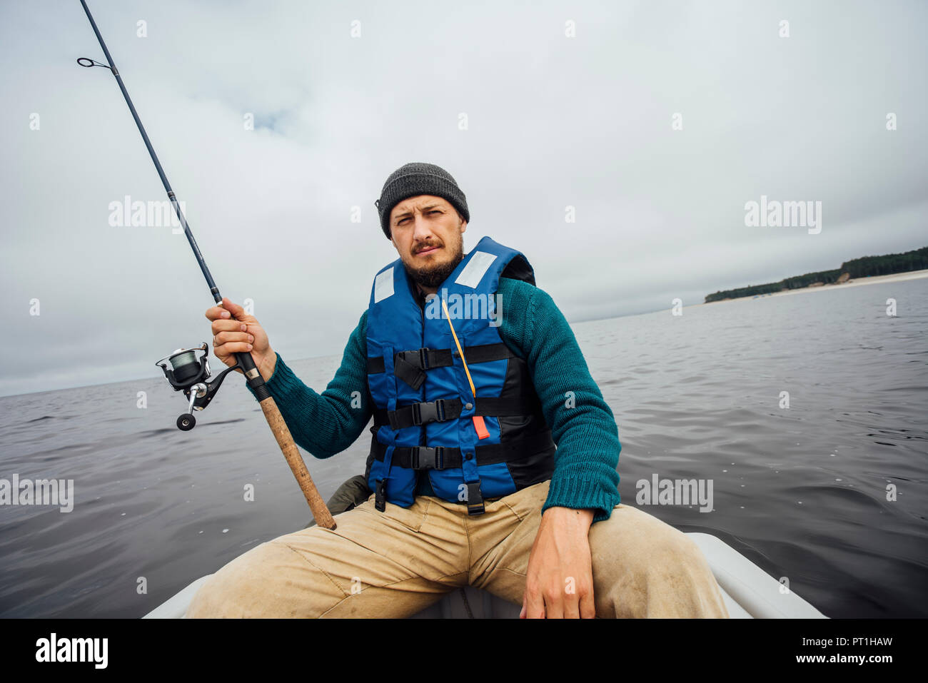Homme assis sur le bateau de pêche avec canne à pêche Banque D'Images
