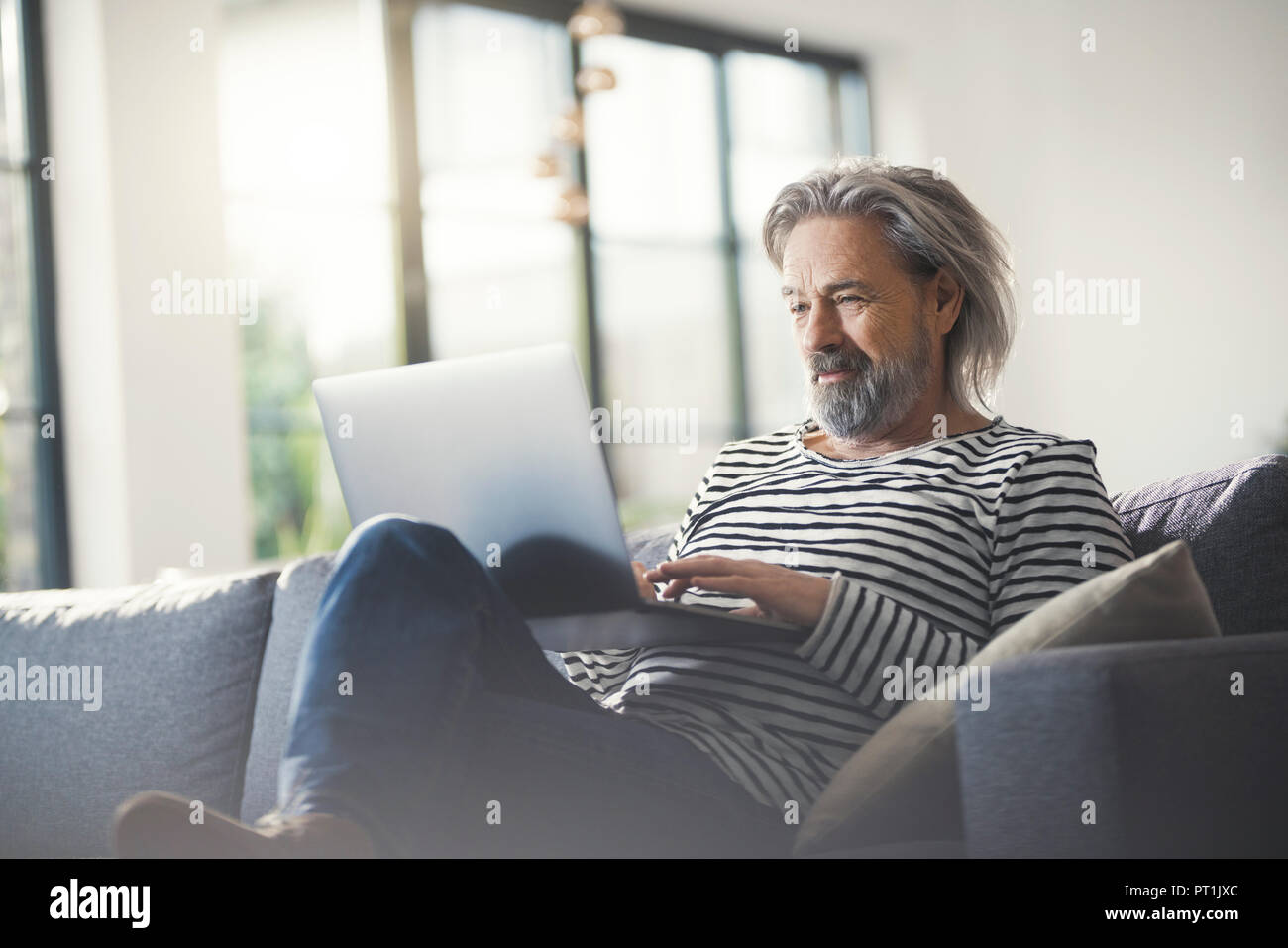 Senior man sitting on couch, using laptop Banque D'Images
