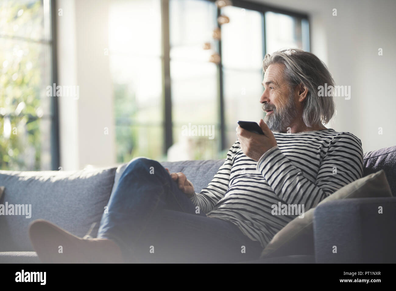 Senior man sitting on couch, using smartphone Banque D'Images