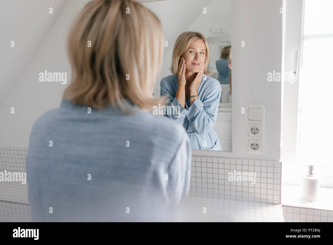 Femme mature à la recherche de miroir de salle de bains Banque D'Images