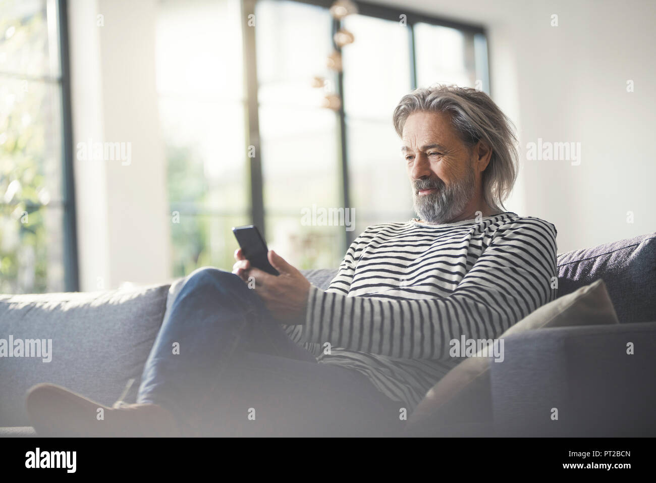 Senior man sitting on couch, using smartphone Banque D'Images