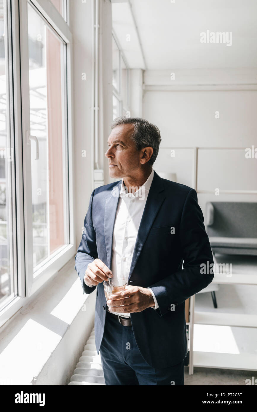 Mature businessman avec verre de café dans son bureau à la fenêtre de Banque D'Images