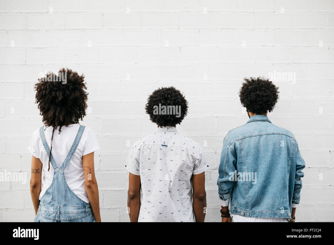Vue arrière de trois amis avec les cheveux bouclés en face de mur blanc Banque D'Images