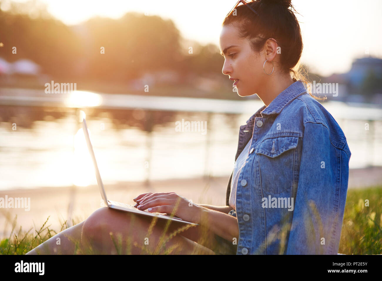 Jeune femme assise sur un pré au crépuscule du soir using laptop Banque D'Images